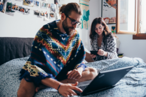 giovane coppia che lavora al proprio business digitale al portatile seduti sul letto matrimoniale